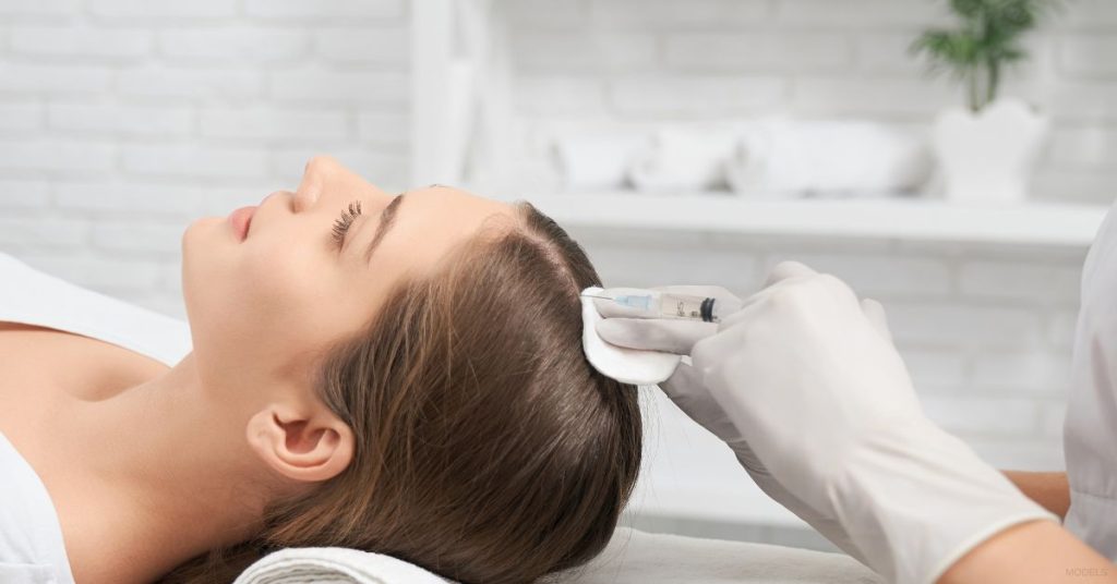 Nurse applying a liquid hair loss treatment to woman's scalp (MODEL)